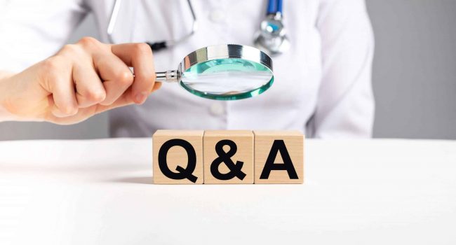 FAQ in health and medicine. Doctor holding magnifier over wooden blocks with letters q a. Woman with stethoscope answers to patients questions about diseases treatment. High quality photo